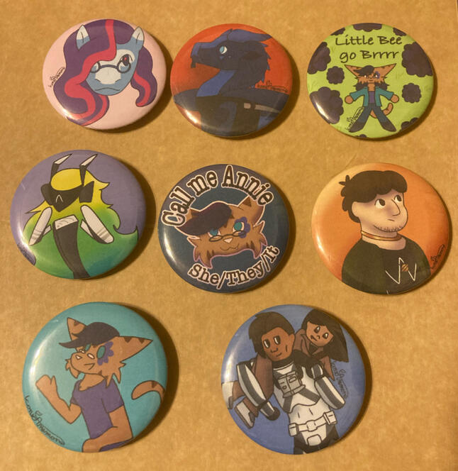 A photo of 8 buttons, all with custom art of original characters