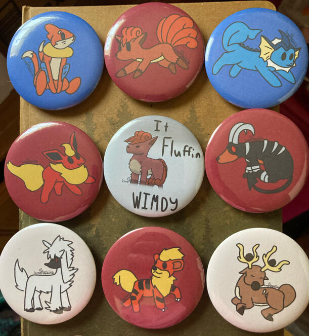 9 pinback buttons in a square. The edge buttons are various pokemon of similar art styles. The middle button is of a vulpix being blown in a snowstorm, with the text “It Fluffen Wimdy”